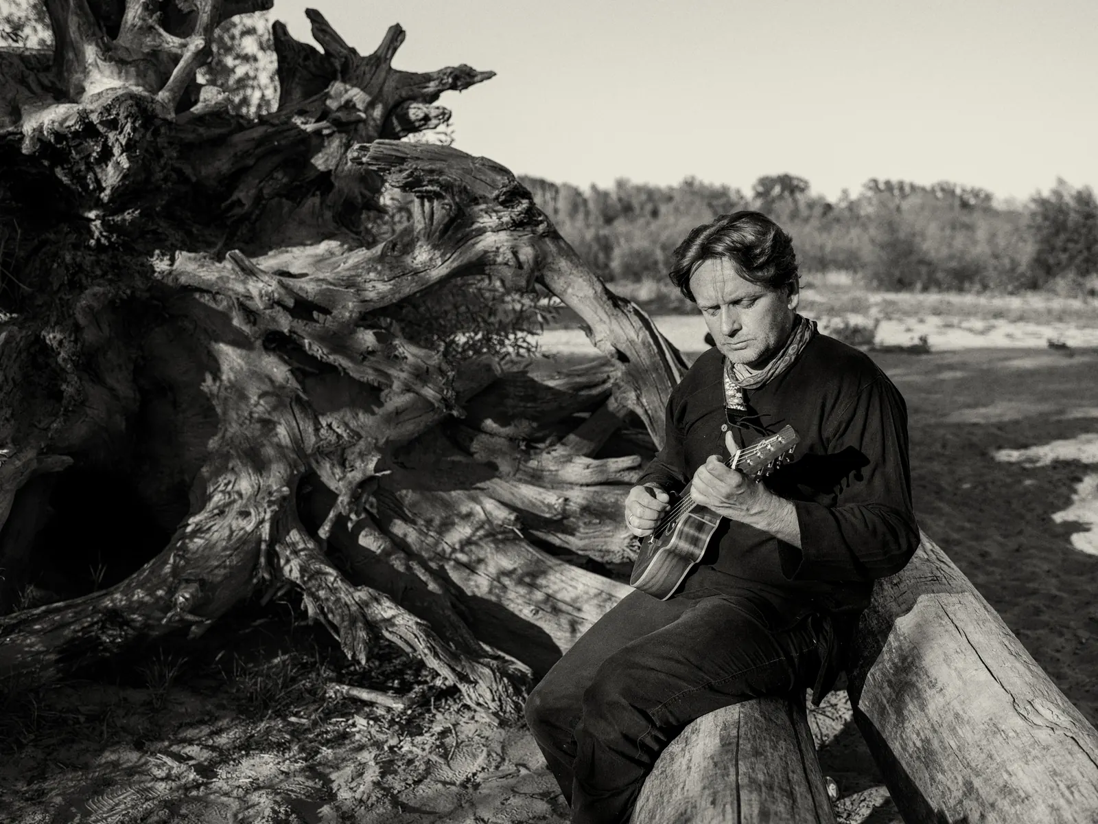 Tomasz Kudelski z ukulele na pniu drzewa nad rzeką